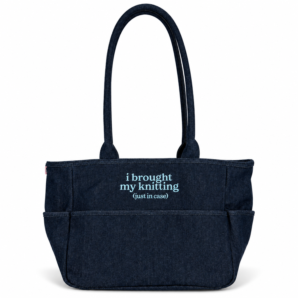 A dark navy blue canvas tote bag with two top handles and a front pocket, featuring the text 'i brought my knitting (just in case)' printed in light blue on the front, set against a plain white background.