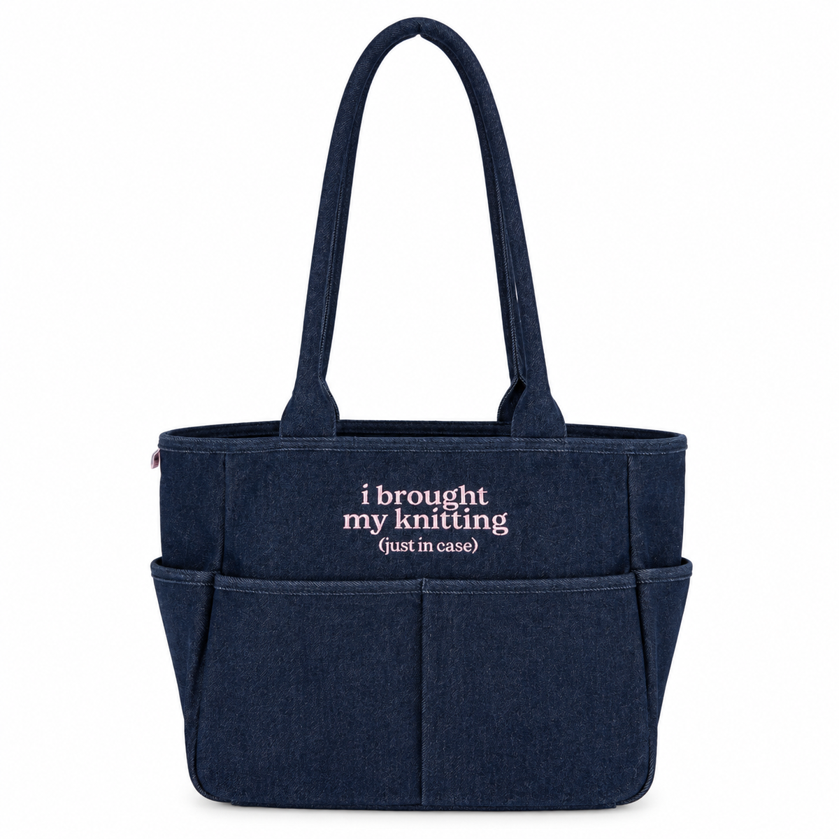 A navy blue canvas tote bag with two top handles and front pockets, featuring the white embroidered text 'i brought my knitting (just in case)' on the front, set against a plain white background.