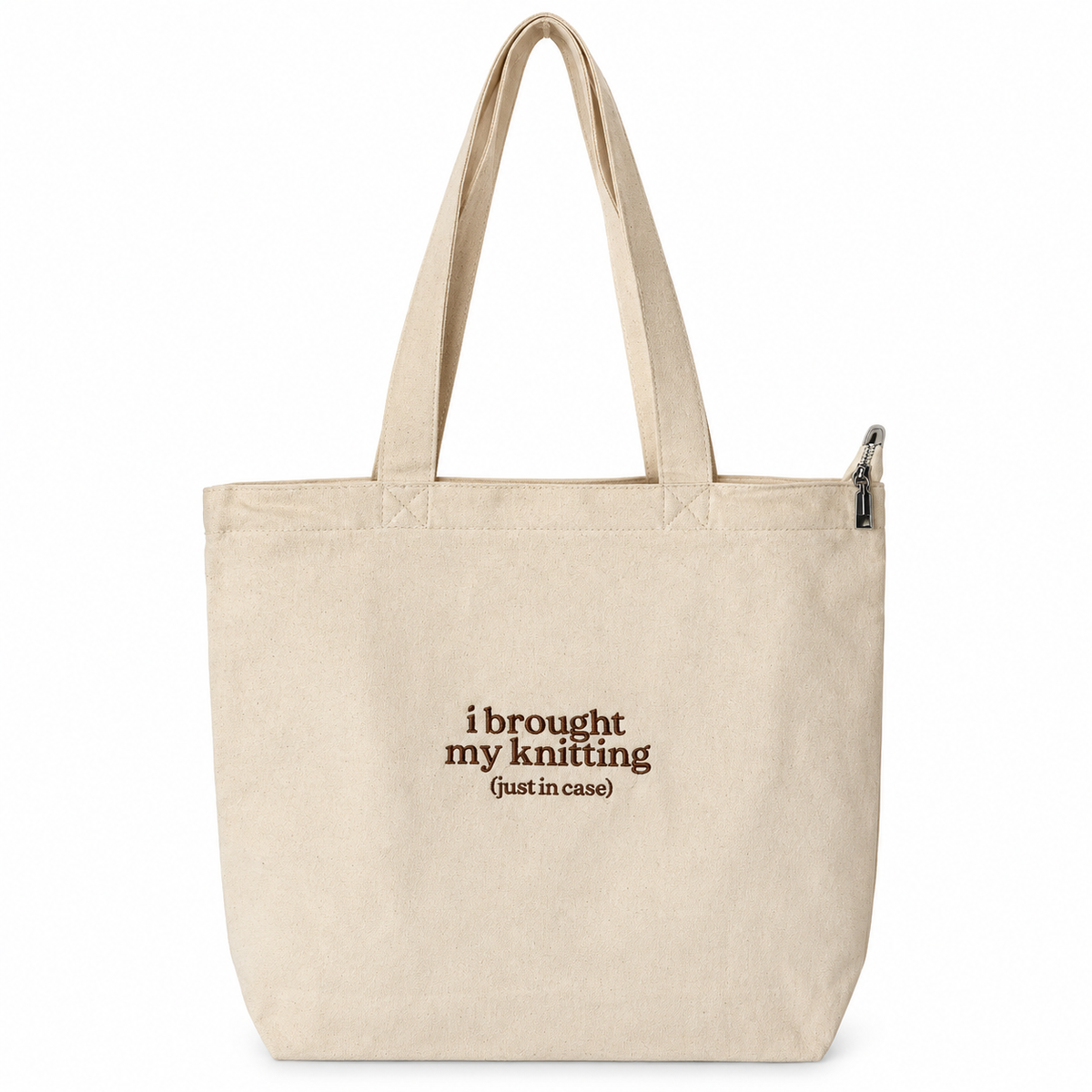 A natural canvas tote bag with two shoulder straps and a top zipper, featuring the printed text 'i brought my knitting (just in case)' in dark brown on the front, set against a plain white background.