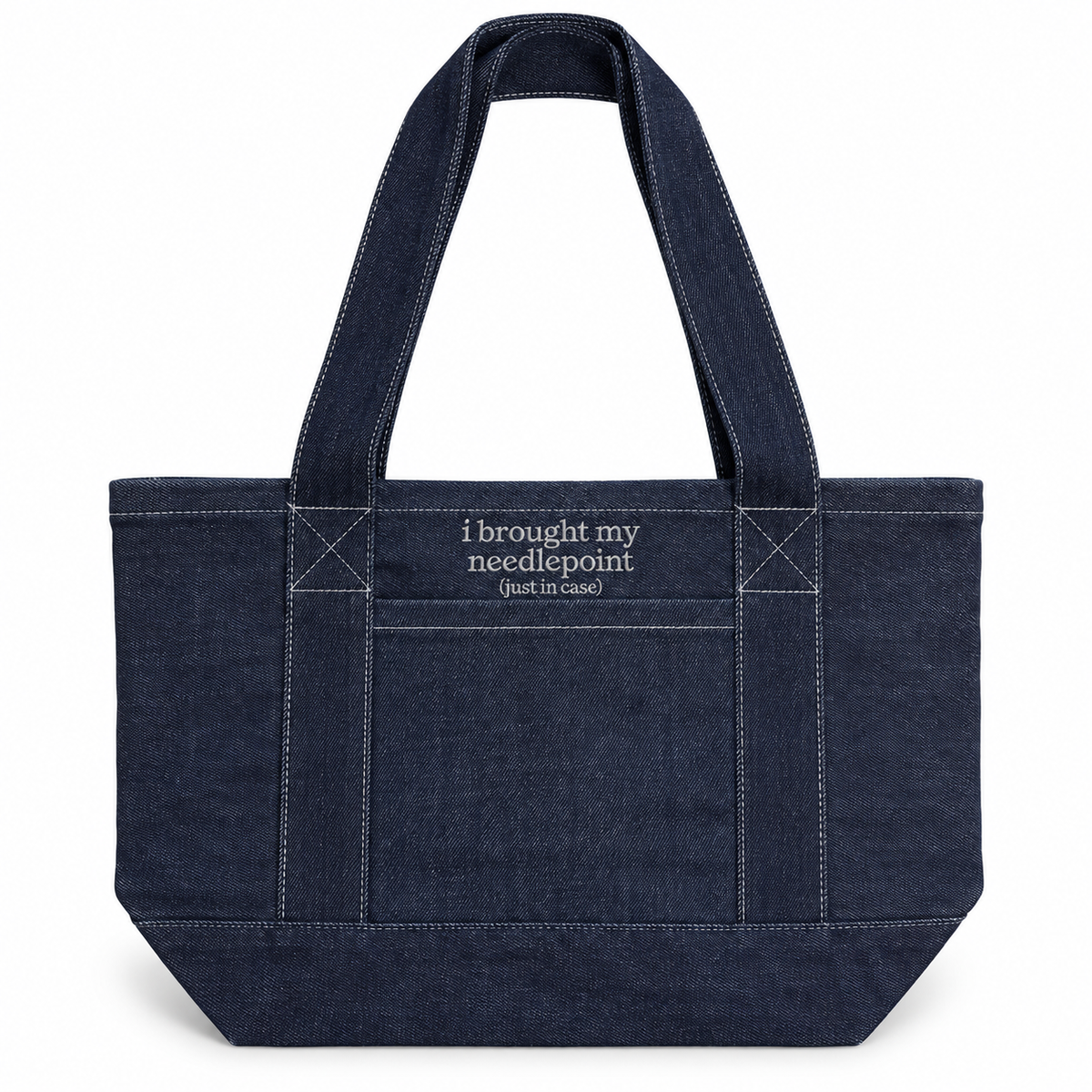A dark navy blue canvas tote bag with white contrast stitching, dual top handles, and white embroidered text on the front pocket that reads 'i brought my needlepoint (just in case)'.