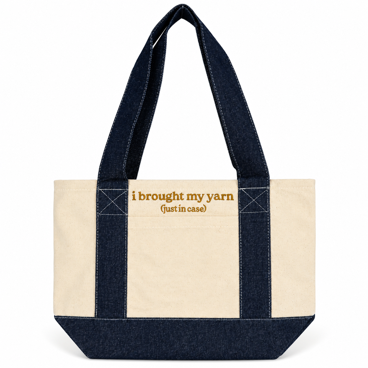 A canvas tote bag with a natural cream body and dark indigo denim straps and base, featuring the text 'i brought my yarn (just in case)' in tan lettering on the front.