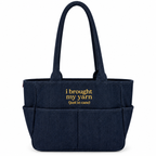 A navy blue fabric tote bag with two shoulder straps, front utility pockets, and yellow embroidered text reading 'i brought my yarn (just in case)'.