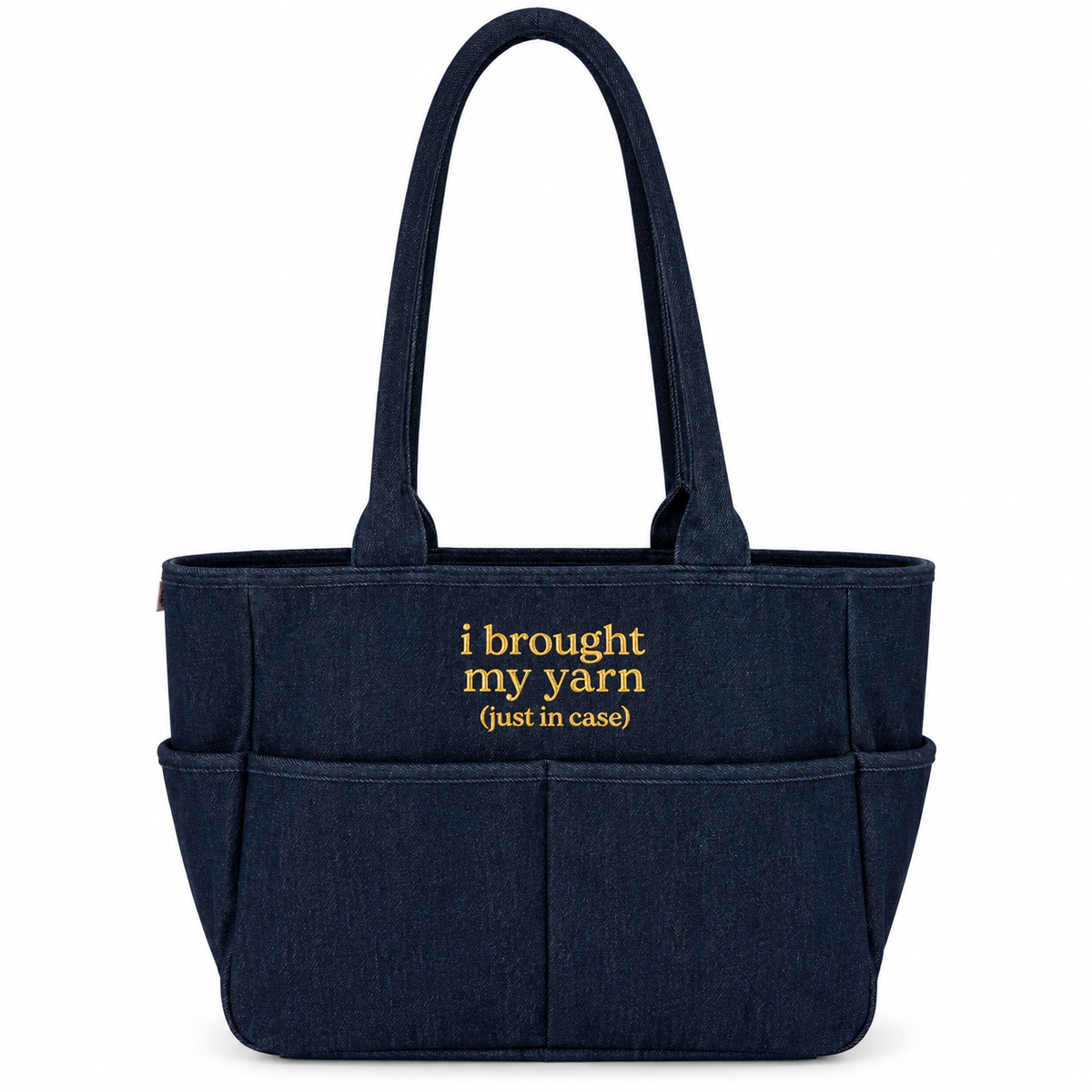 A navy blue fabric tote bag with two shoulder straps, front utility pockets, and yellow embroidered text reading 'i brought my yarn (just in case)'.