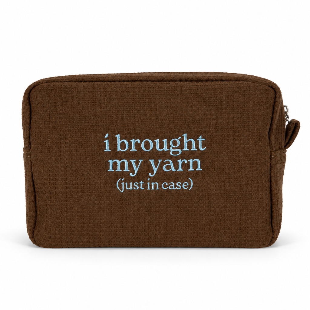 A brown textured zippered pouch with the phrase 'i brought my yarn (just in case)' printed in light blue text on the front, shown against a plain white background.