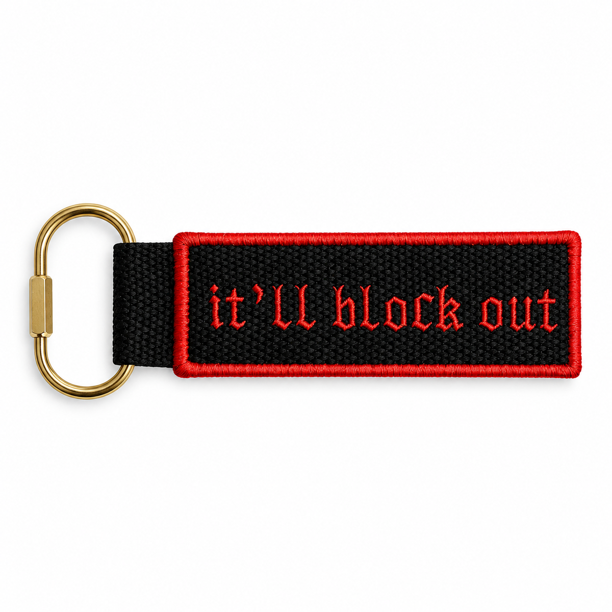 Black bag charm with red border and red gothic “It’ll Block Out” embroidery, attached to a gold clip.