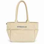 A beige canvas tote bag with dual top handles and the phrase 'it'll block out' printed in navy blue text on the front, set against a plain white background.