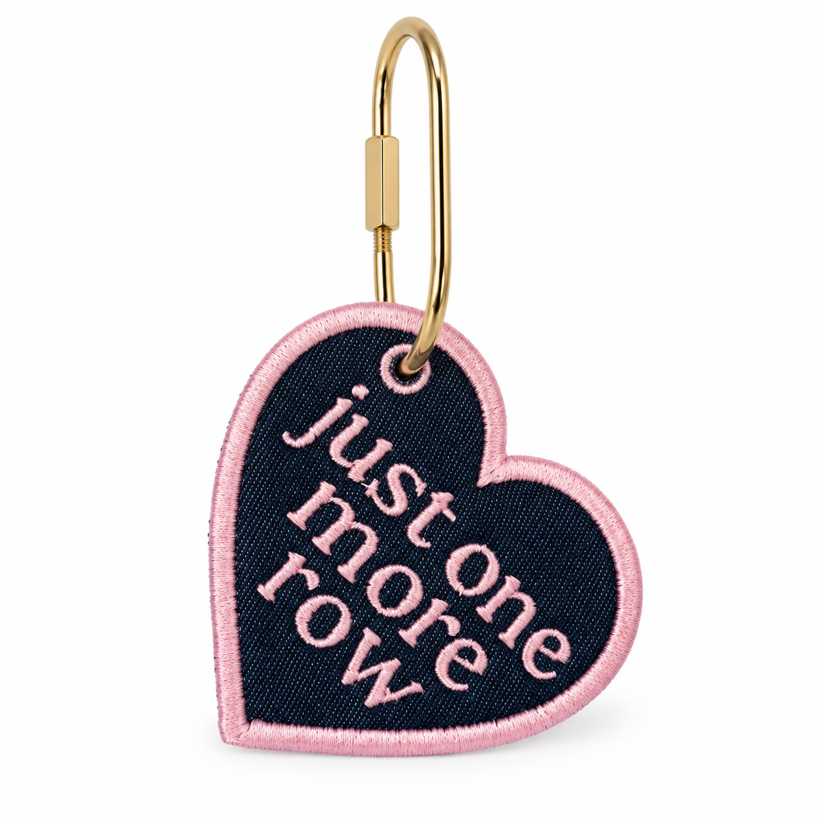 A heart-shaped embroidered patch with a gold metal clip, featuring the phrase 'just one more row' in pink script on a dark navy blue background with a pink border.