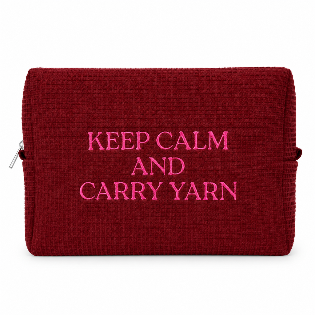 A dark red textured waffle-weave zippered pouch with bright pink embroidered text reading 'KEEP CALM AND CARRY YARN' on a white background.