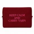 A dark red textured waffle-weave zippered pouch with bright pink embroidered text reading 'KEEP CALM AND CARRY YARN' on a white background.