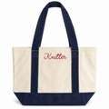 A canvas tote bag with an off-white body, dark navy blue handles and bottom trim, and red embroidered text reading 'Knitter' on the front pocket, shown on a plain white background.
