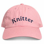 A pink cotton baseball cap with the word 'Knitter' embroidered in navy blue script across the front, shown on a clean white background.