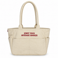 A natural canvas tote bag with two top handles and front pockets, featuring the red embroidered text 'KNOT YOUR AVERAGE HOOKER' on the front, set against a plain white background.