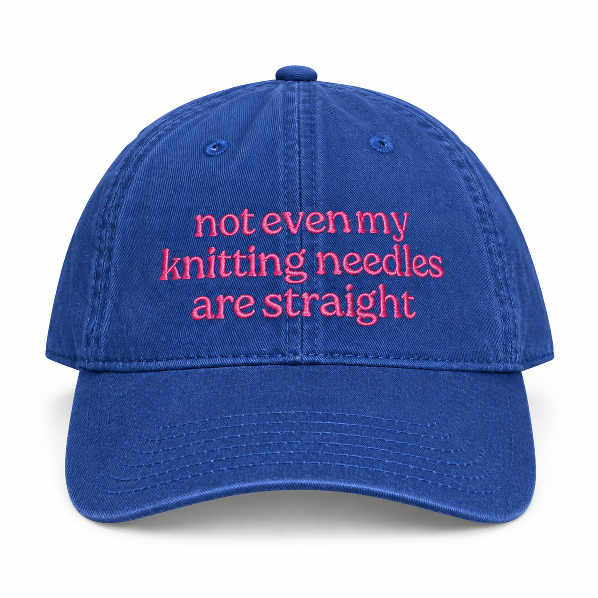 A blue cotton baseball cap with pink embroidered text on the front that reads 'not even my knitting needles are straight', shown against a plain white background.