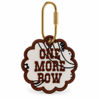 An embroidered keychain tag with a scalloped edge, featuring the text 'ONE MORE ROW' in brown on a cream background with a black-and-white striped pattern, attached to a gold carabiner.