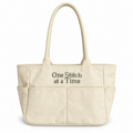 Natural canvas TIMI Tote with dark olive “One Stitch at a Time” cross stitch embroidery.