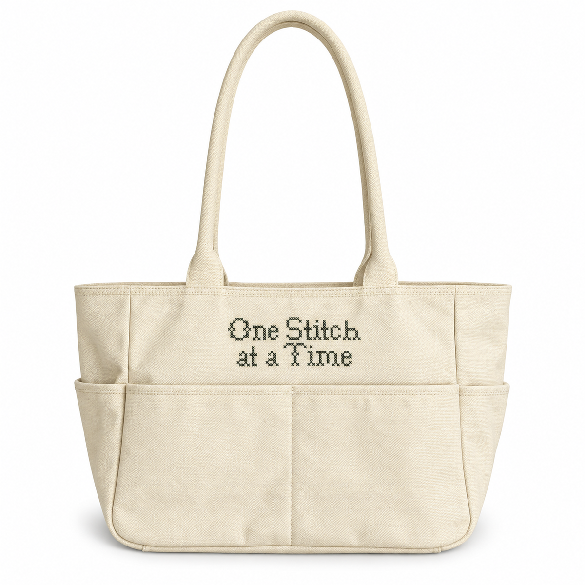 Natural canvas TIMI Tote with dark olive “One Stitch at a Time” cross stitch embroidery.