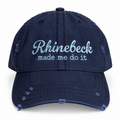 A navy blue distressed baseball cap with light blue embroidered text reading 'Rhinebeck made me do it' on the front, shown against a plain white background.