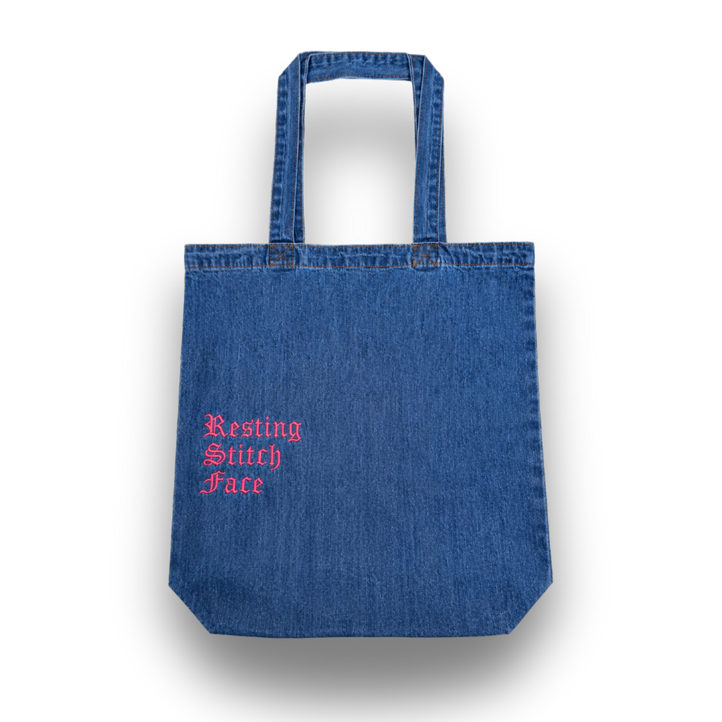Blue denim tote bag with 'Resting Stitch Face' text in pink on a white background