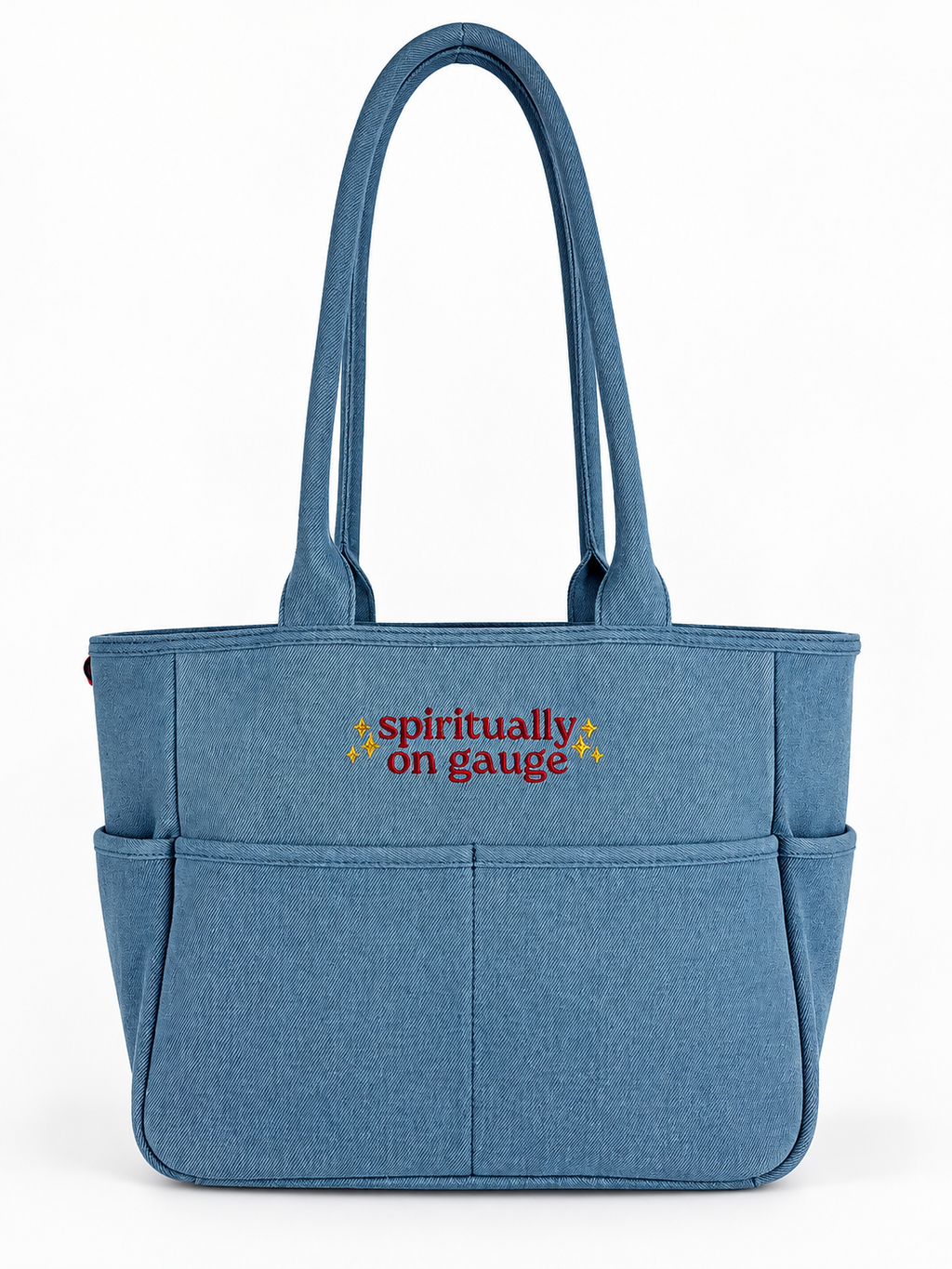 A blue fabric tote bag with dual shoulder straps, front utility pockets, and the text 'spiritually on gauge' embroidered in red and yellow on the front, shown against a plain white background.