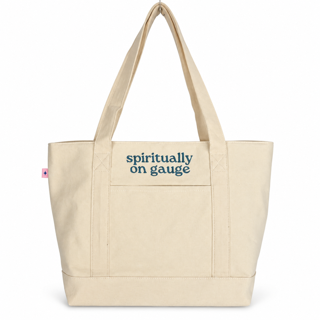 A natural canvas tote bag with dark blue text reading 'spiritually on gauge' on the front pocket, shown against a plain white background.