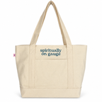A natural canvas tote bag with dark blue text reading 'spiritually on gauge' on the front pocket, shown against a plain white background.