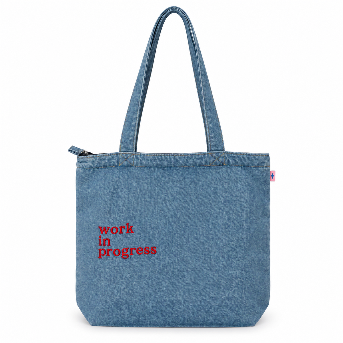 A blue denim tote bag with 'work in progress' printed in red text on the front, shown against a plain white background.