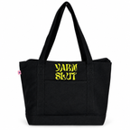 A black canvas tote bag with two shoulder straps and a front pocket, featuring the words 'YARN SLUT' printed in a stylized yellow font on the front pocket. A small pink tag is visible on the left side seam.