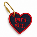 Denim heart bag charm with red “Yarn Slut” gothic embroidery and gold-tone clip.